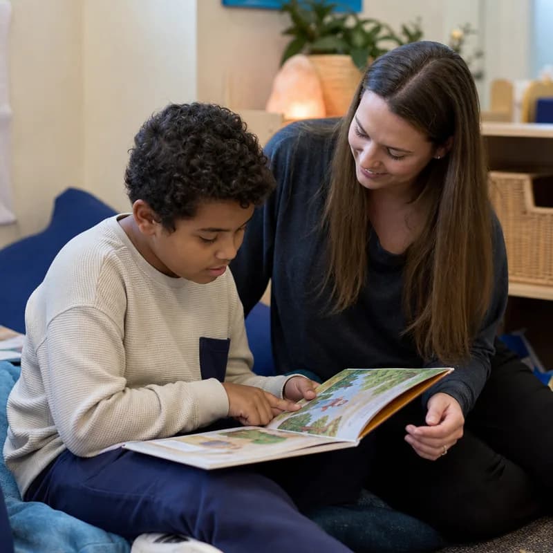 Autistic child reading a picture book with a supportive educator in a quiet reading corner