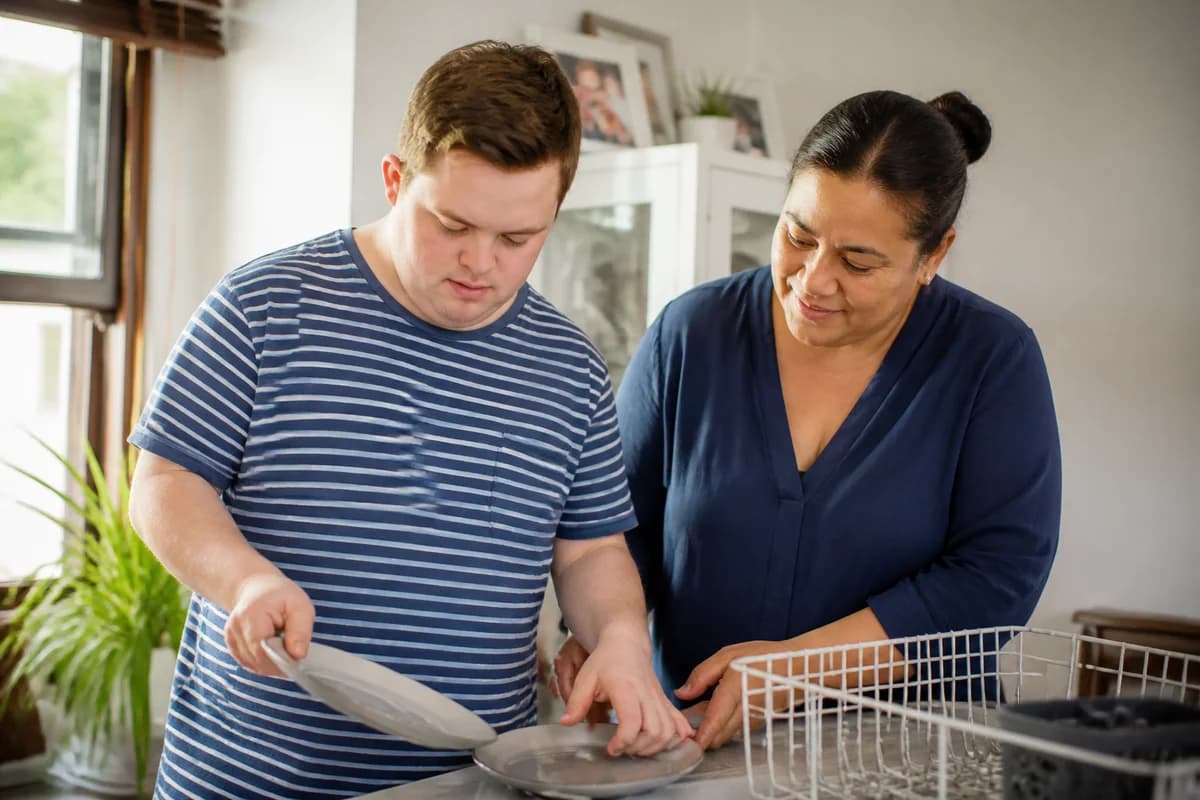 Support worker gently helping a young adult with an everyday kitchen life skill at home